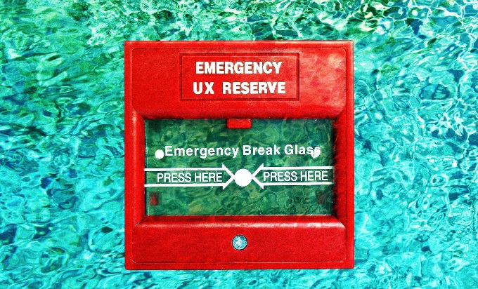 A red fire alarm behind a bright blue water background. The glass on the fire alarm says, "Emergency Break Glass," and printed on the alarm it reads, "Emergency: UX Reserve."